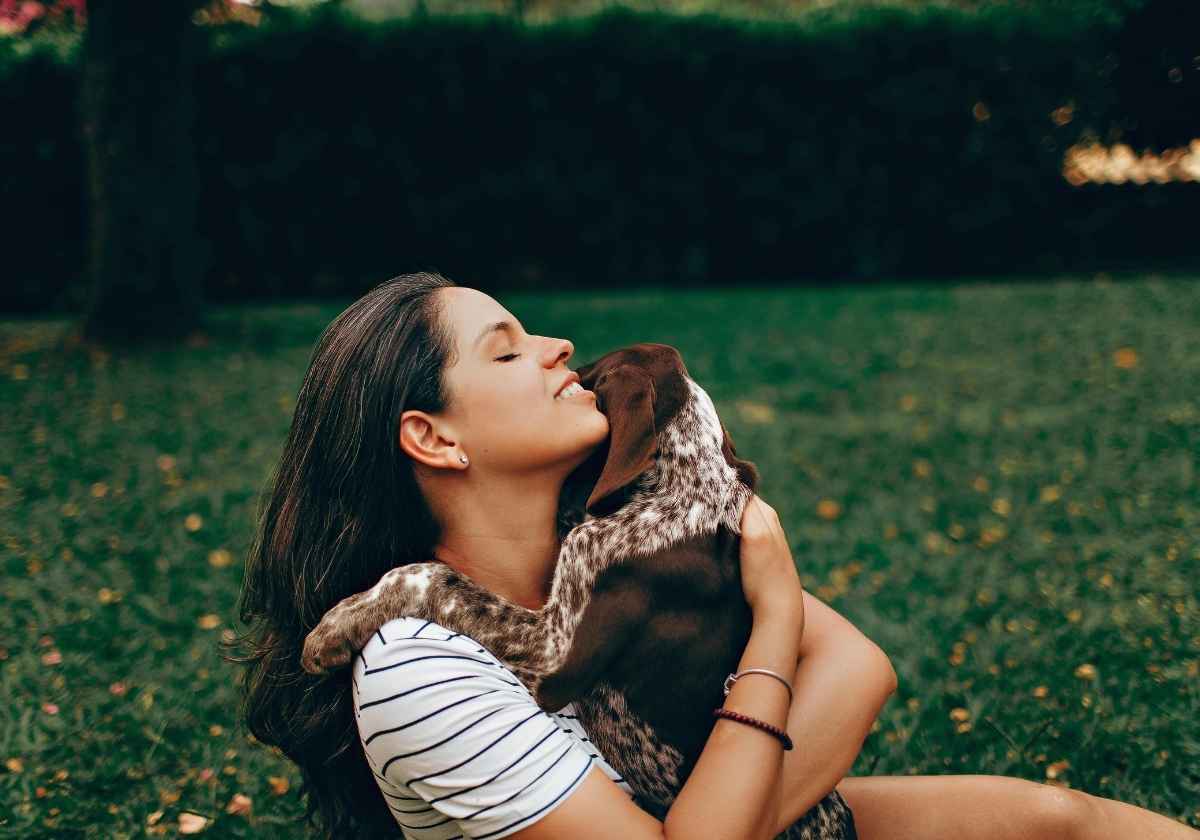 Woman embracing spotted dog outdoors.